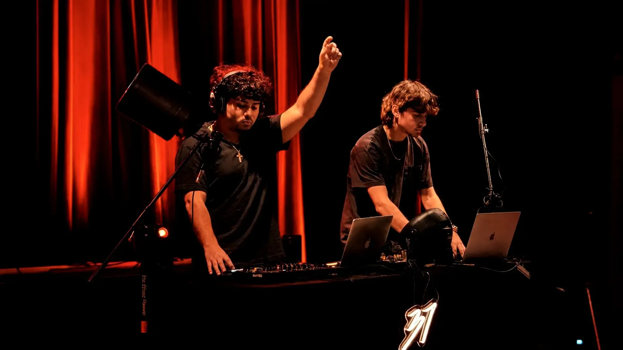 Two DJs playing a set, headphones on and hands on the controller