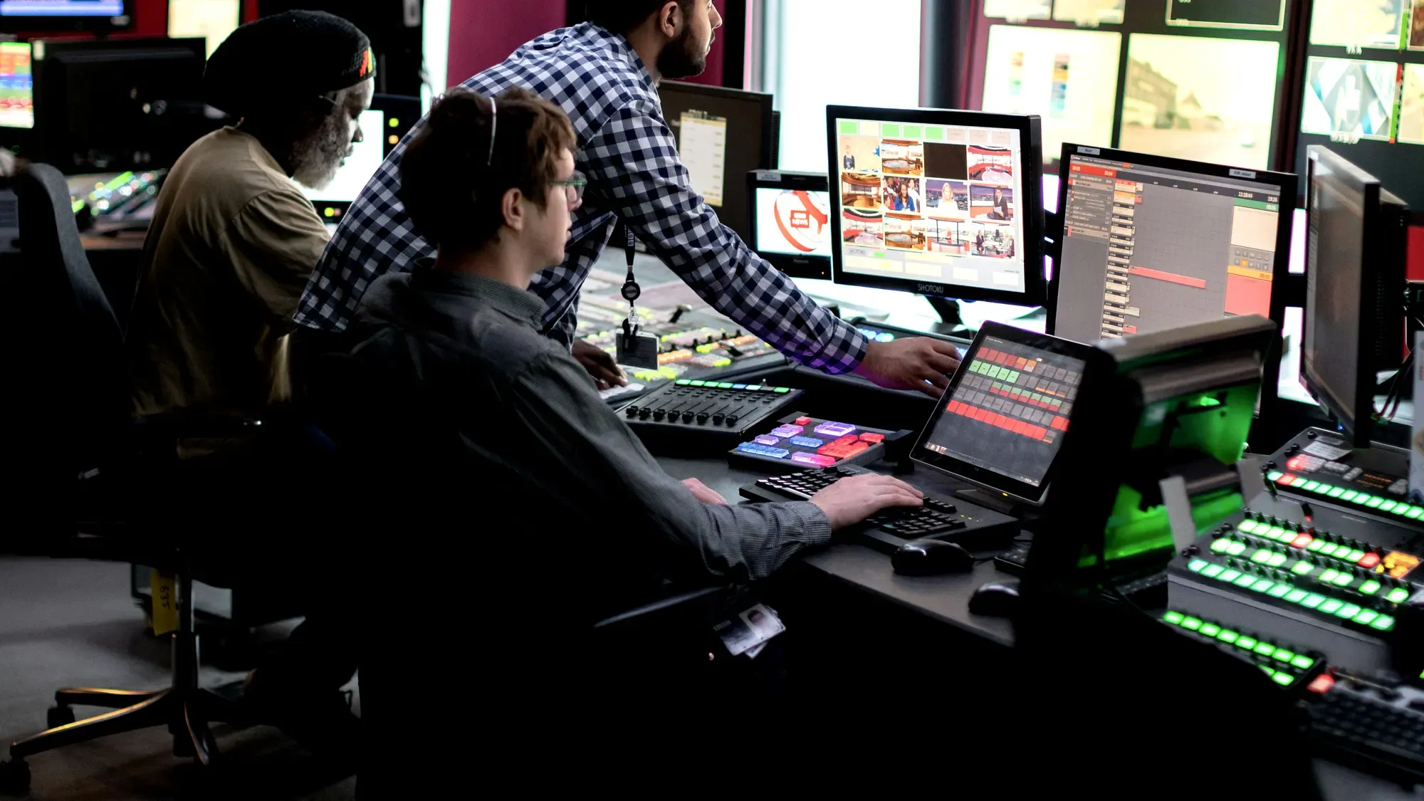 Three operators at a vision desk in front of a monitor wall