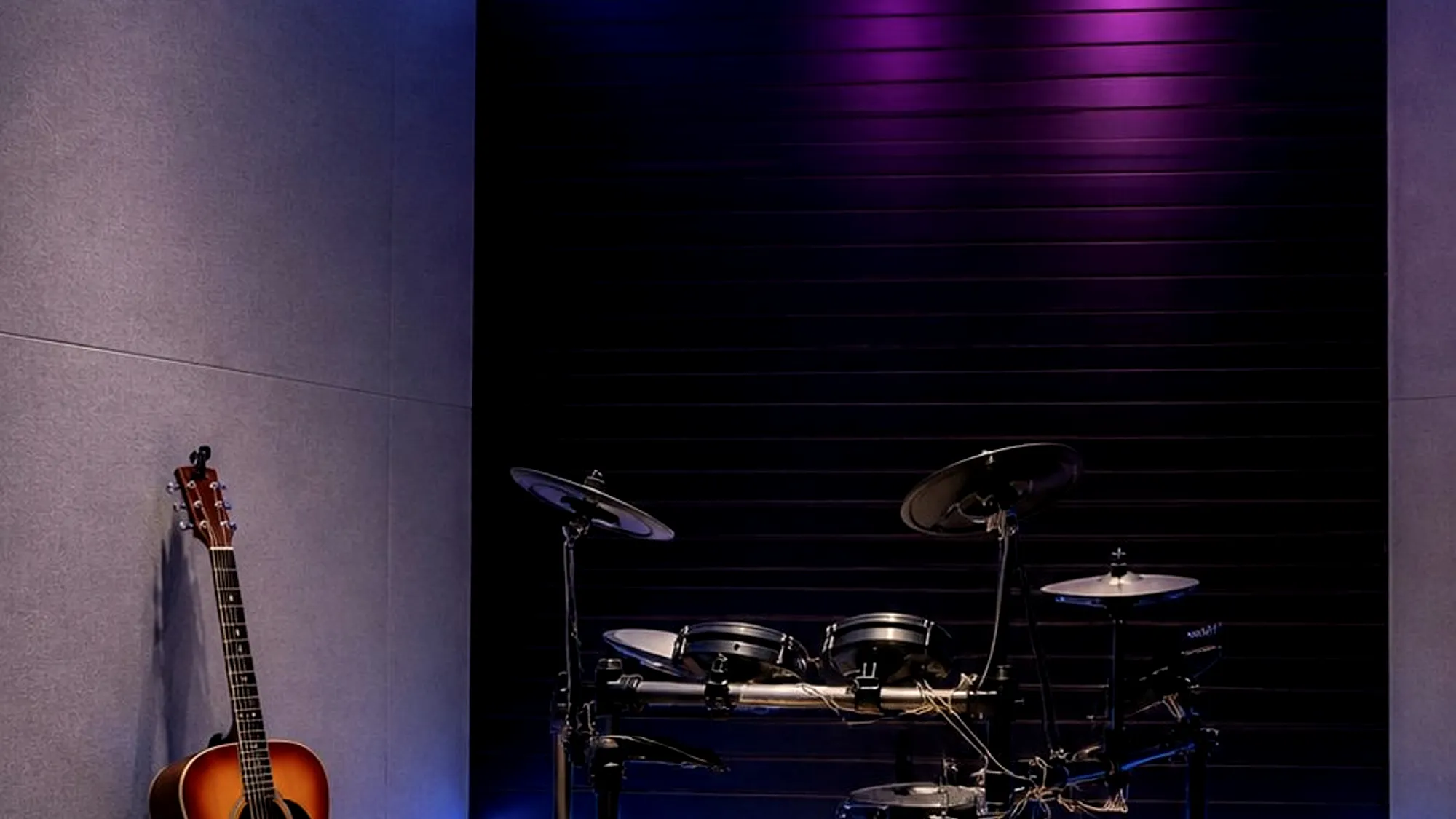 The live room: an acoustic guitar against the wall and a drum kit under purple light