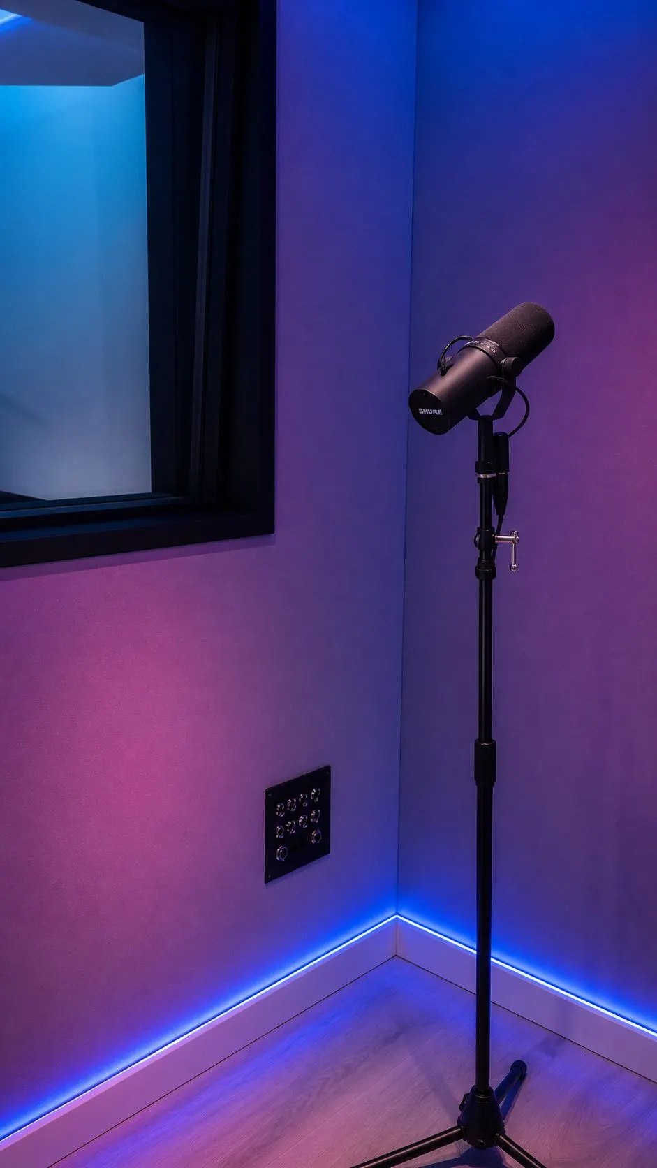 A Shure SM7B on a stand in the vocal booth beside a wall panel of XLR tie lines